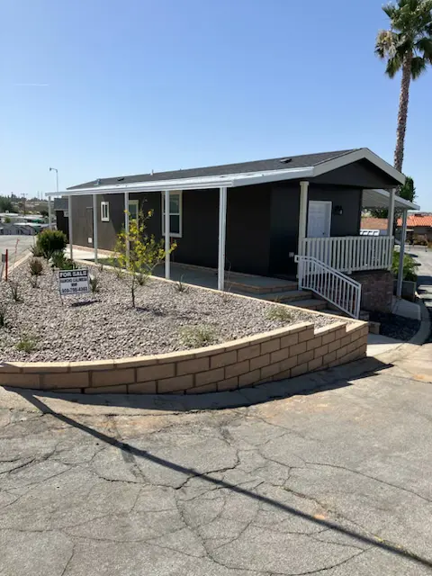 The 2026 Skyline home for sale, a dark grey exterior with a covered carport and a for-sale sign in the rock bed
