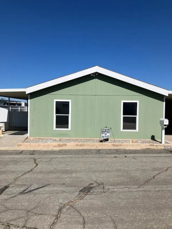 The home for sale at Space 216, a green exterior with a carport and a for-sale sign